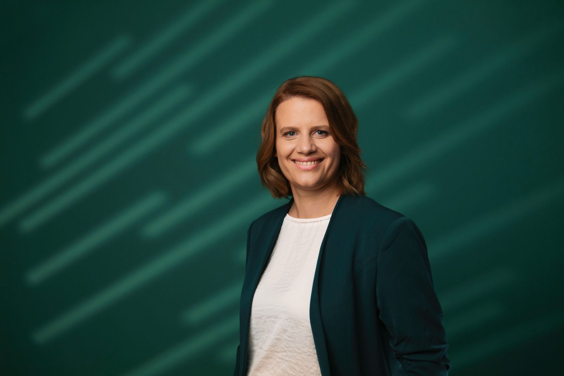 Julia Willie Hamburg lächelt in die Kamera, sie trägt einen dunklen Blazer vor dunkelgrünem Hintergrund.